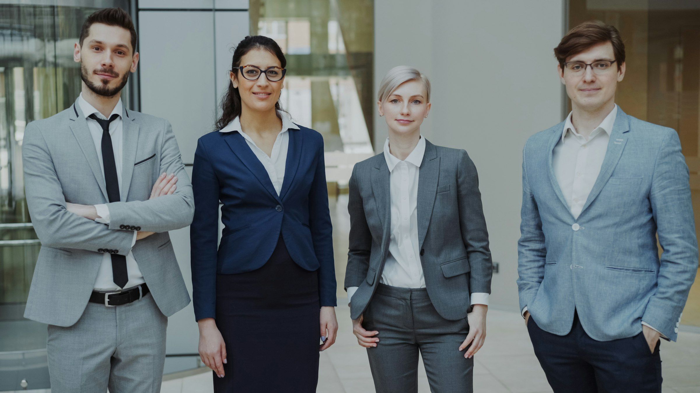 Four people in formal business attire standing side by side in an office lobby.